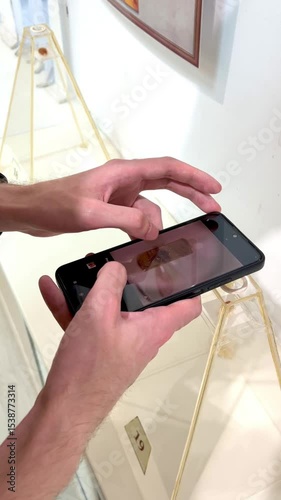 Person uses smartphone camera to capture detailed image of art piece in gallery