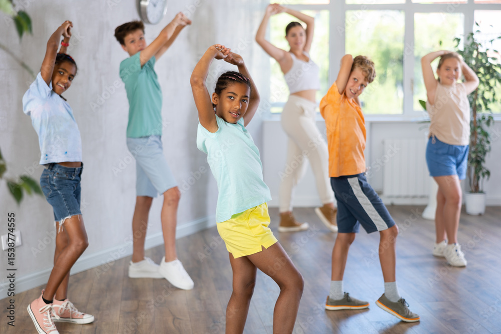 Naklejka premium Group of positive juvenile boys and girls engaged in sport dances in training room together with young trainer