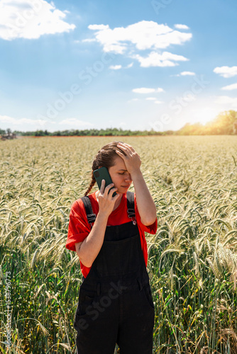 farming problems. Female farmer reacting to phone call in cereal field with hand on forehead