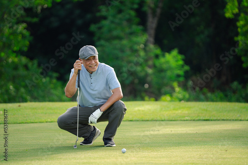 Fotografía Senior golfer crouching on green grass, focusing on golf ball alignment before putting