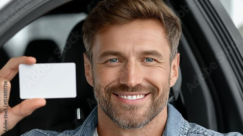 Smiling man holding a blank card while sitting in a car, showcasing confidence and casual style.