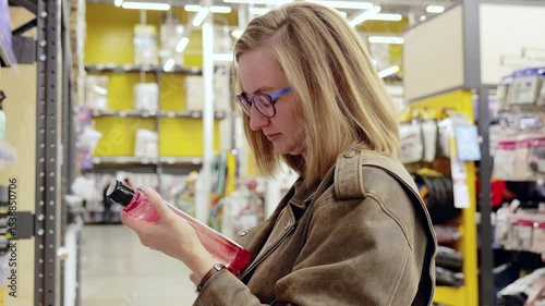 Young woman selecting hair care products while shopping in a supermarket. Browsing through various shampoo bottles, she reads labels for informed decisions