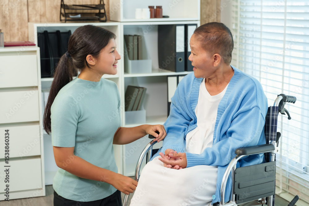 Obraz premium Young Asian woman offers emotional support and encouragement to elderly woman in wheelchair, smiling warmly and engaging in a positive conversation during recovery process.