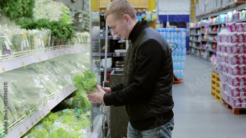 Young customer is choosing fresh produce at the supermarket. He is standing in the produce aisle and is holding a bag of lettuce. Buying fresh herbs at the supermarket