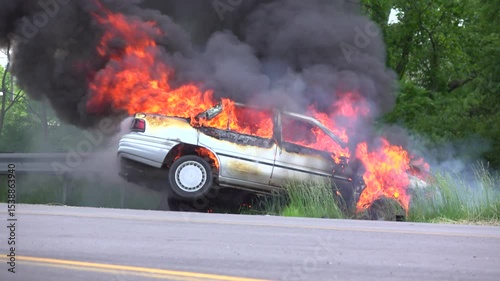 Flames coming from burning car on side of road.
