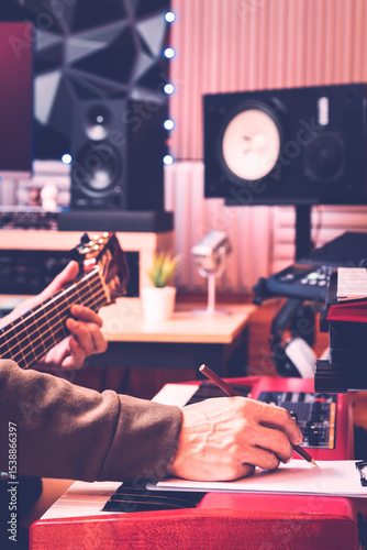 male musician hands writing a hit song by playing acoustic guitar and electric piano in home recording studio. songwriting, music education concept