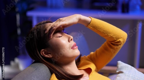 Video 4k of Asian woman is resting on the sofa looking unwell with a headache and fever. She appears stressed tired and exhausted from cold flu or illness at home