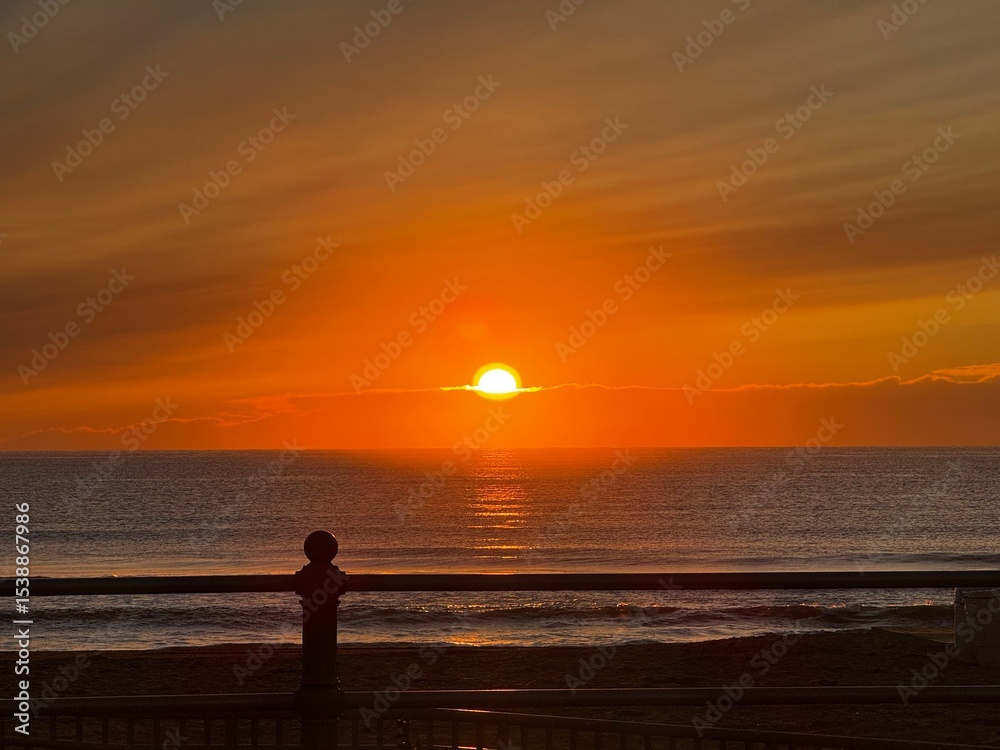 Fototapeta premium Golden sunrise over calm Atlantic waters at Virginia Beach with soft reflections and silhouetted railing