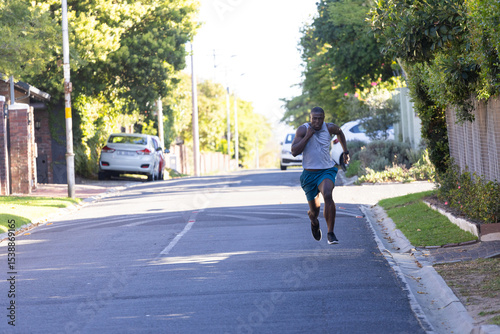 Wallpaper Mural African American man sprinting on tree-lined street wearing tank top with white towel, copy space Torontodigital.ca