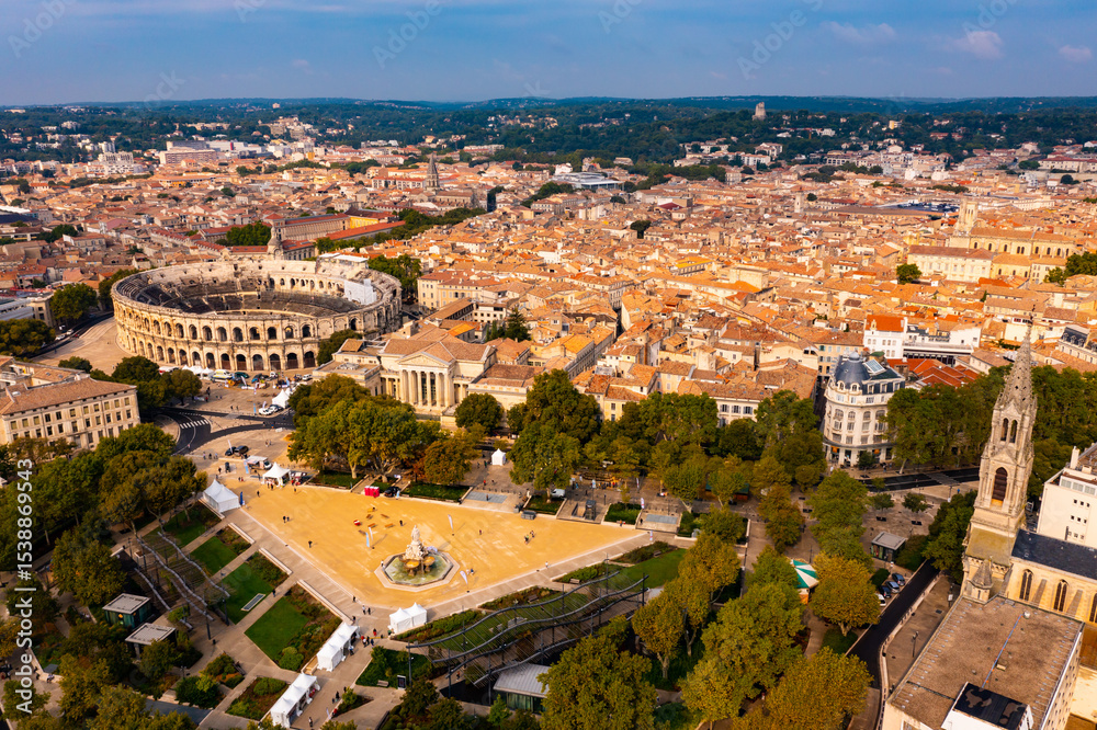 Naklejka premium Drone view of ancient Roman amphitheatre Arena of Nimes on background of reddish tiled roofs of residential buildings on summer day, France