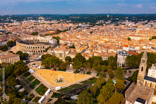 Drone view of ancient Roman amphitheatre Arena of Nimes on background of reddish tiled roofs of residential buildings on summer day, France photo