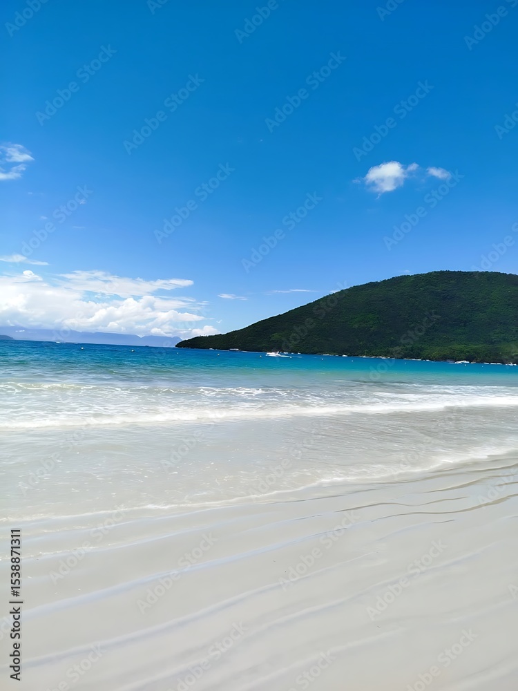 Obraz premium A scenic view of a Ubatuba tropical beach with white sand, blue water, and a lush green hill under a clear blue sky