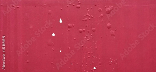 The red painted cement wall has blistered paint marks. A blistered colored film protruding from the wall may be a sac of water or air. The background of the red painted wall has blistered paint marks.