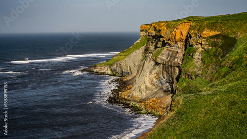 Eroding cliffs and green meadows meet the North Sea under a cloudy sky in Whitby, a coastal town in North York Moors National Park, UK