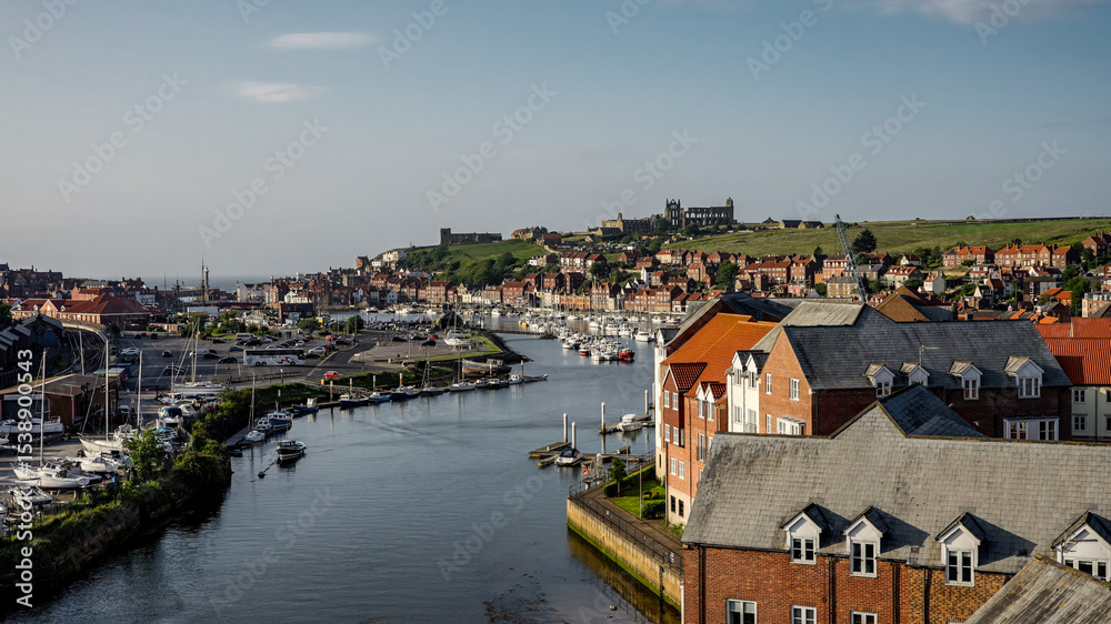 Obraz premium Scenic view of Whitby harbor in North Yorkshire, featuring Saint Mary's Church and boats on the River Esk on a sunny summer day