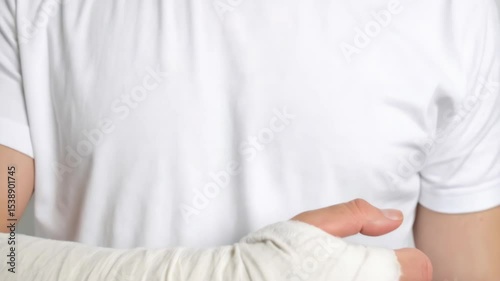 Person wearing a white t-shirt showing a broken arm entirely covered in a white plaster cast, isolated on a neutral background.