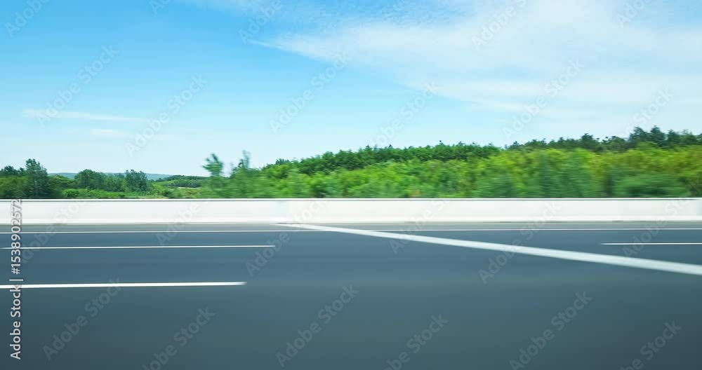 Driving on an asphalt highway with white lane markings alongside a dense green forest. Driving on an asphalt highway with white lane markings alongside a dense green forest.