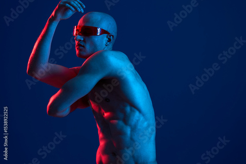Half-naked man with sunglasses striking a dynamic pose against a blue background, showcasing a blend of vibrant light and shadow, emphasizing physical fitness.