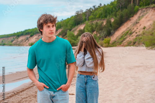 A young couple quarreling on the beach, the guy in the foreground and the upset girl crying behind him