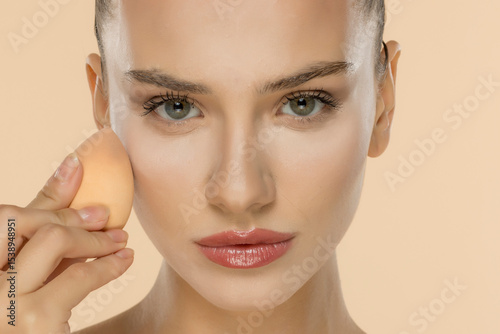 Professional makeup application with beauty sponge, showcasing flawless skin and precise cosmetic technique