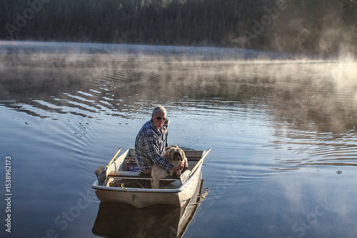 Elderly man and his dog cruising in a small fiberglass fishing boat with an electric motor on Elk River Reservoir in Idaho