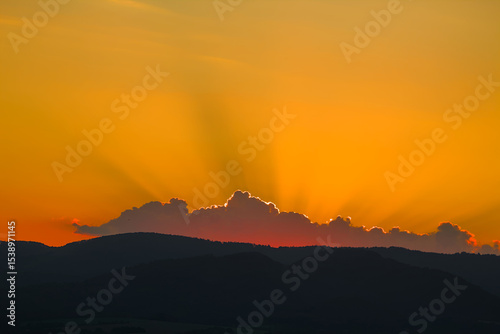 Intense golden sunset with sun rays over silhouetted hills.