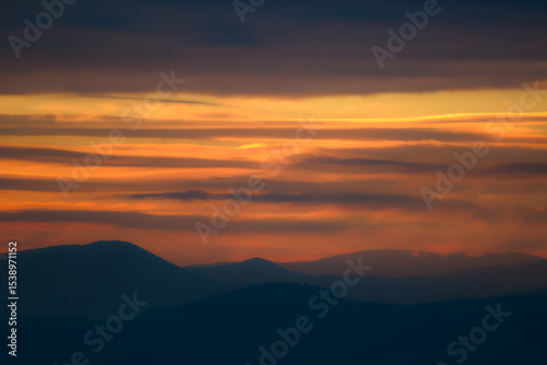 Beautiful layered sunset clouds in orange and purple over mountains.