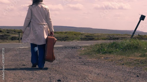 Woman walking with suitcase in empty highway road