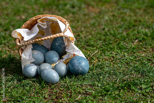 Colorful eggs in a woven basket on green grass during a sunny day
