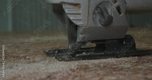Close-up of a jigsaw cutting through oriented strand board, creating flying sawdust particles with professional skill. A man uses a jigsaw to cut through an osb sheet.
