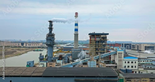 Large thermal power plant with smoking chimneys and industrial equipment in a heavy industry zone by a river.