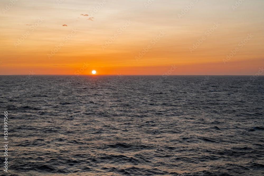Fototapeta premium A breathtaking sunset over a calm sea, with the sky painted in warm hues of orange, pink, and purple. Gentle waves reflecting the golden sunlight. A peaceful, serene atmosphere