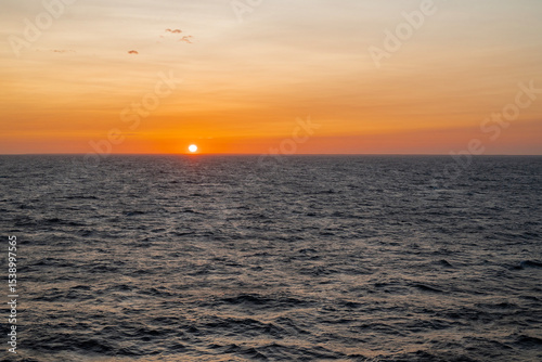 A breathtaking sunset over a calm sea, with the sky painted in warm hues of orange, pink, and purple. Gentle waves reflecting the golden sunlight. A peaceful, serene atmosphere