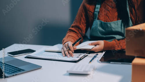 Startup SME small business entrepreneur of freelance Asian woman wearing apron using laptop and box to receive and review orders online to prepare to pack sell to customers, online sme business ideas.