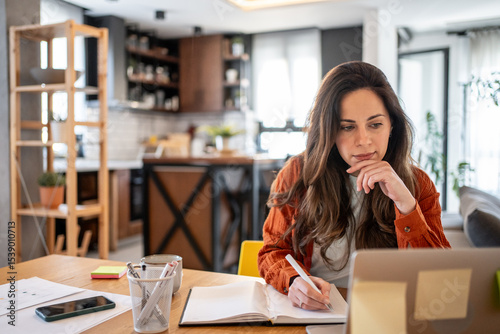 Bilde på lerret Focused freelancer working from home taking notes from laptop