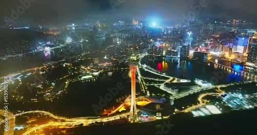 Macau cityscape and its iconic tower brightly illuminated at night with city lights reflecting on the water.