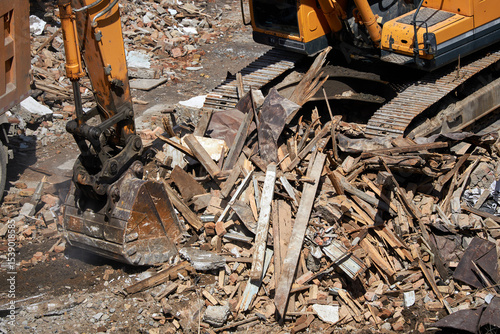 Excavator stands on rubble of house. Dismantling process, demolition of old building, destruction of dilapidated housing.