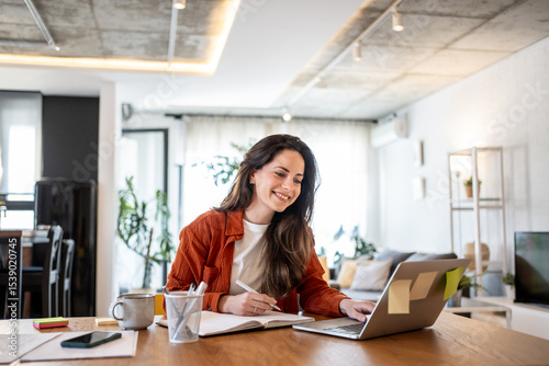 Foto Freelancer working from home using laptop and taking notes