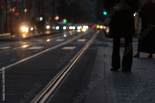 As night falls, the city comes alive with illuminated tram tracks, colorful traffic lights, and bustling pedestrians, creating a vibrant atmosphere that captivates the senses