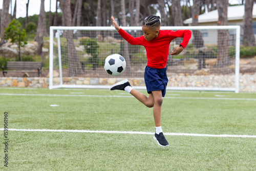 Young boy skillfully kicking soccer ball on outdoor field, showing athletic talent