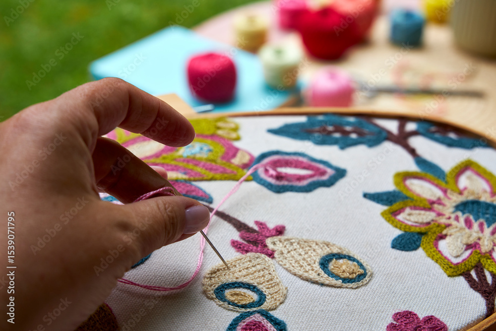 Fototapeta premium Front close-up view of a woman's hands embroidering a decorative pattern on fabric stretched in an embroidery hoop. The hands are focused and steady, with visible stitches forming on the fabric. Natur