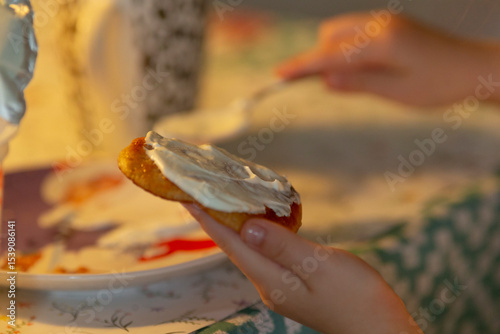 A childs small hands are carefully spreading icing on a freshly baked cookie using a knife, all set in a cozy kitchen environment, filled with the aroma of baking goodies