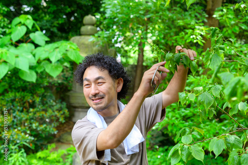 木々に囲まれた庭で剪定作業中の男性が笑顔で自然と向き合う穏やかな庭仕事のひととき