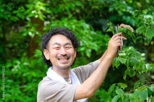 男性が木の枝に剪定ばさみを向けながらにこやかに作業する夏の庭仕事のひととき photo