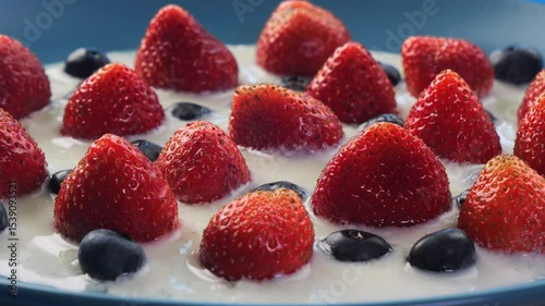 Strawberries and blueberries berries in heavy cream rotating in a circle on a blue background. Medium shot.