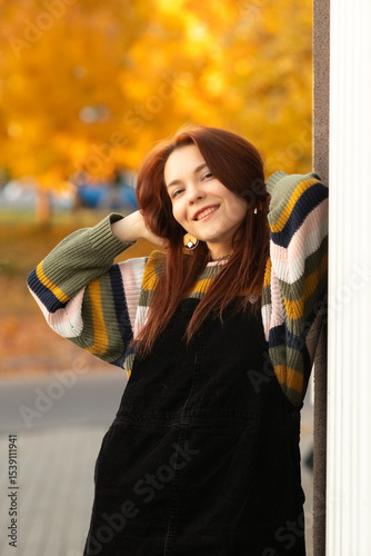 Portrait of a young beautiful red-haired girl in an autumn city park.