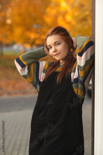 Portrait of a young beautiful red-haired girl in an autumn city park.