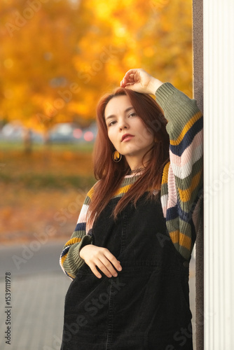 Portrait of a young beautiful red-haired girl in an autumn city park.
