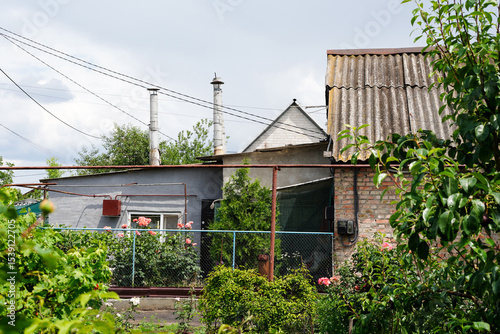 A rustic countryside house with a tin roof and brick walls stands behind a lush green garden filled with rose bushes