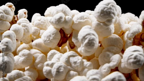 Freshly popped popcorn fills the frame in a close-up macro shot on empty black background. Fluffy white kernels with golden brown accents create a delicious texture. Concept of snack food, movie time,